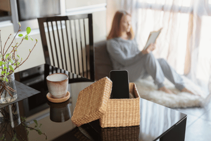 Frau liest ein Buch während das Handy auf dem Tisch liegt.