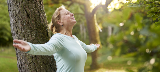 Frau mit weit geöffneten Armen vor einem Baum