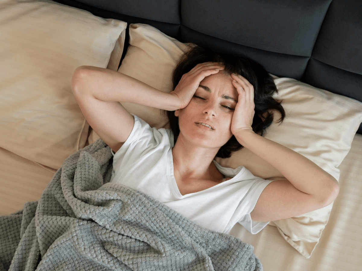 Frau liegt mit starken Kopfschmerzen im Bett.